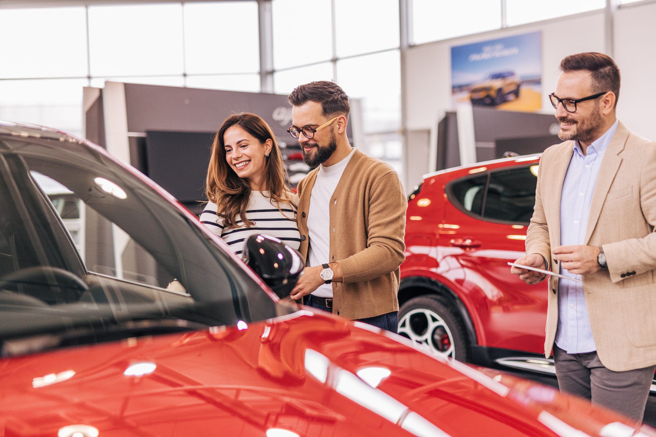 A sales agent helping an adult couple choose a new car in a modern car showroom